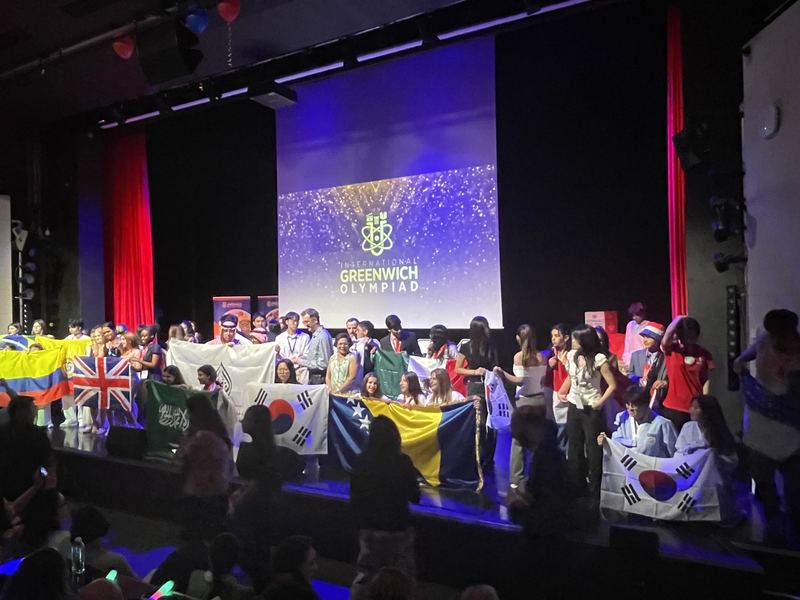 Finalists with national flags on stage at the International Greenwich Olympiad awards ceremony