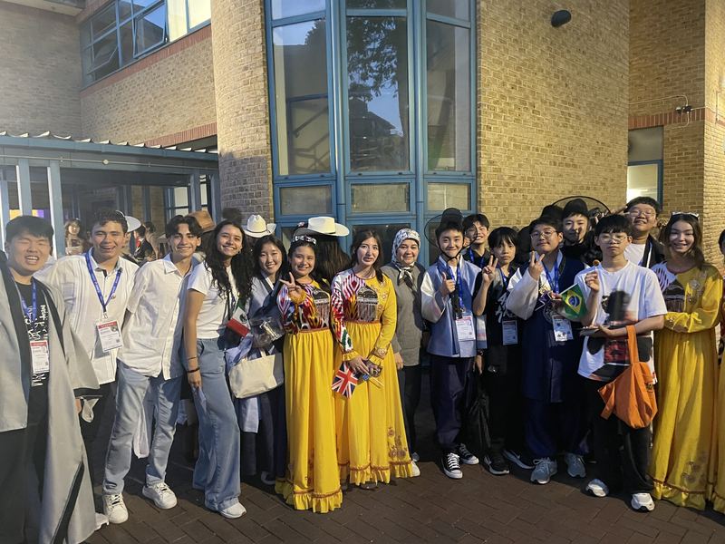Students in traditional dress from different countries posing together at night
