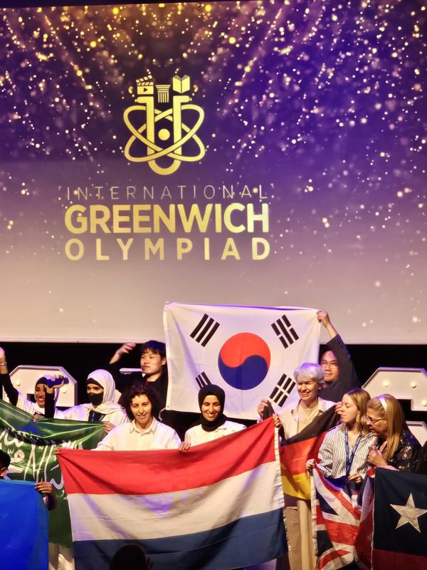 Students raising the Korean flag on stage under the International Greenwich Olympiad logo
