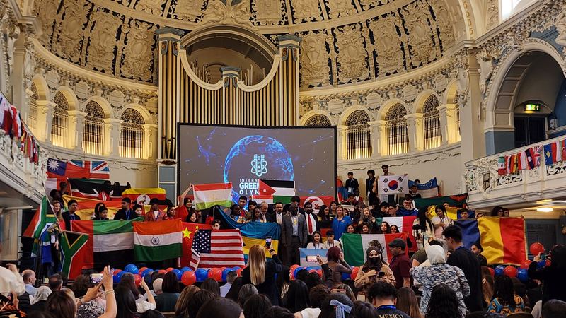 Students waving flags from many countries at the opening ceremony in an ornate hall