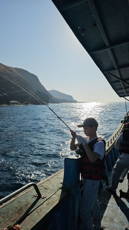 Mark fishing from a boat beside sea cliffs